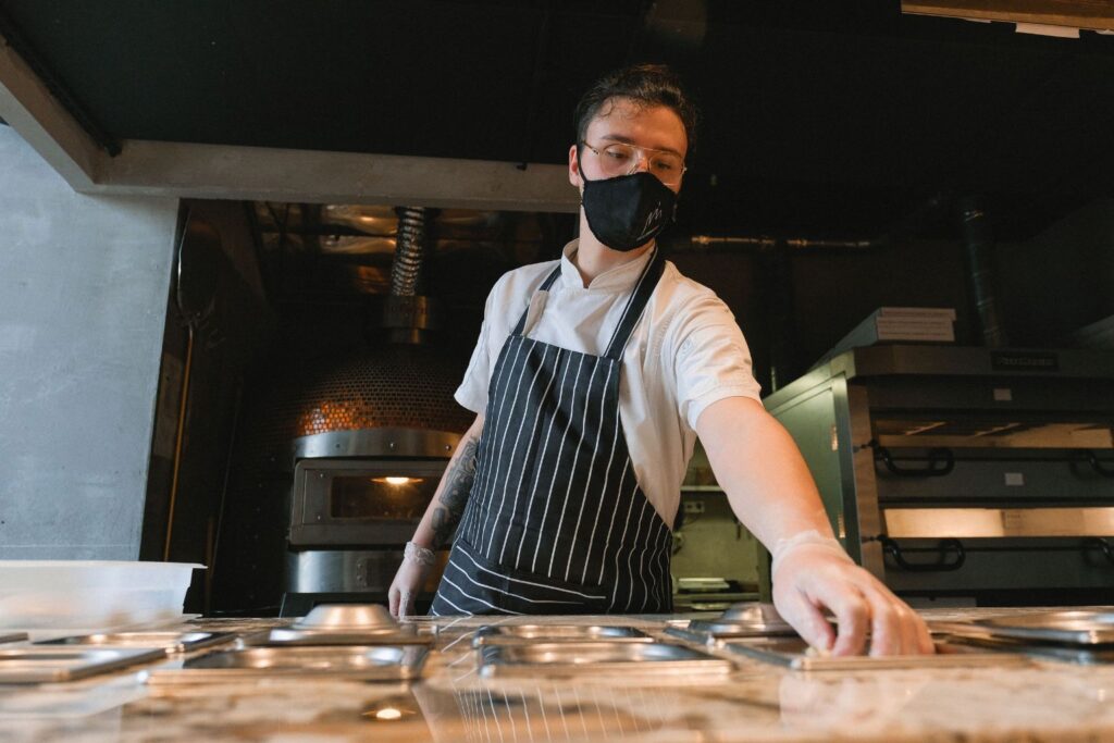 Restaurant cook wearing a mask at a pizza station